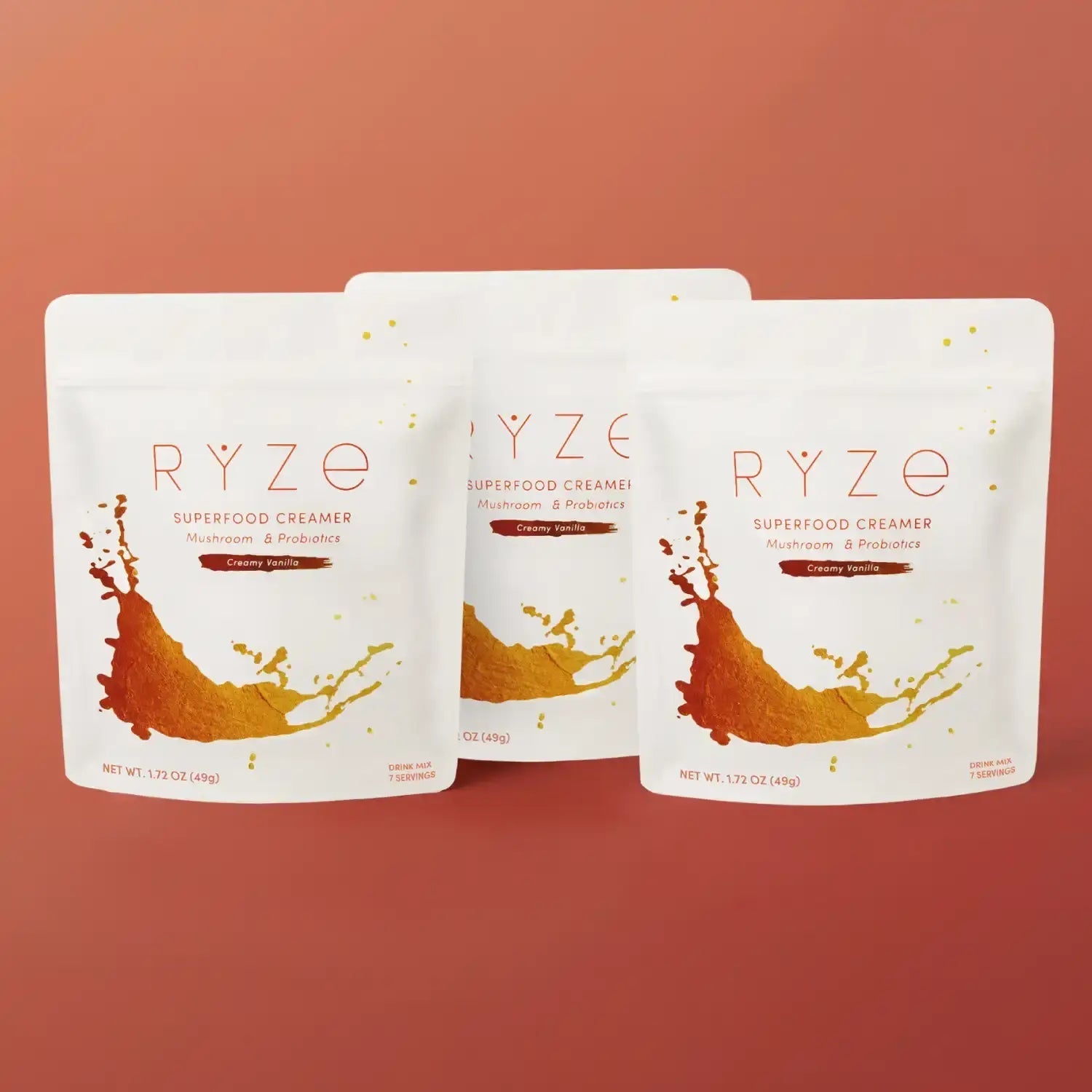 Three RYZE Superfood Creamer Creamy Vanilla bags (white with orange splash design) displayed on a terracotta background